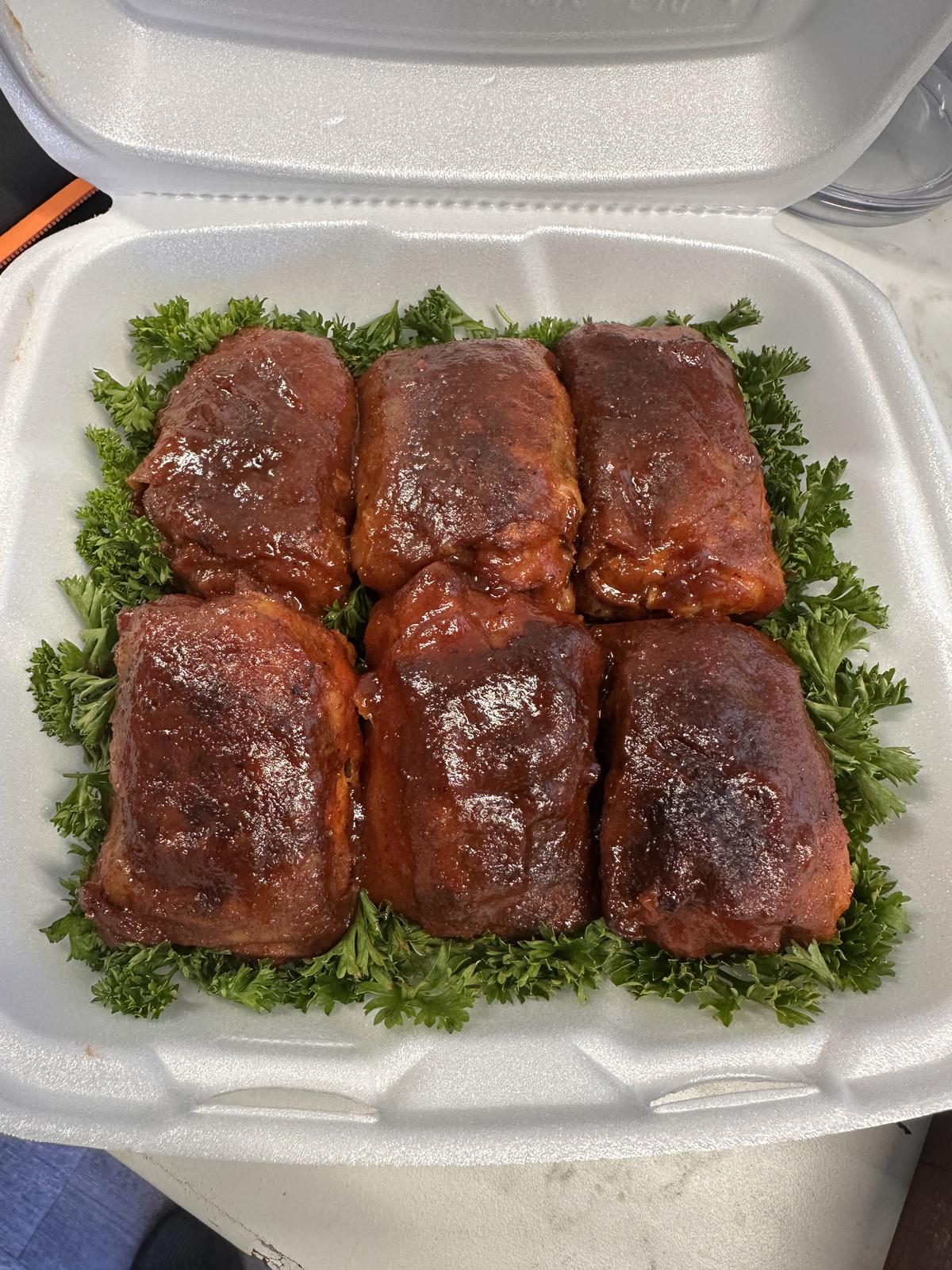 Six glazed chicken thighs arranged on parsley in a takeout box