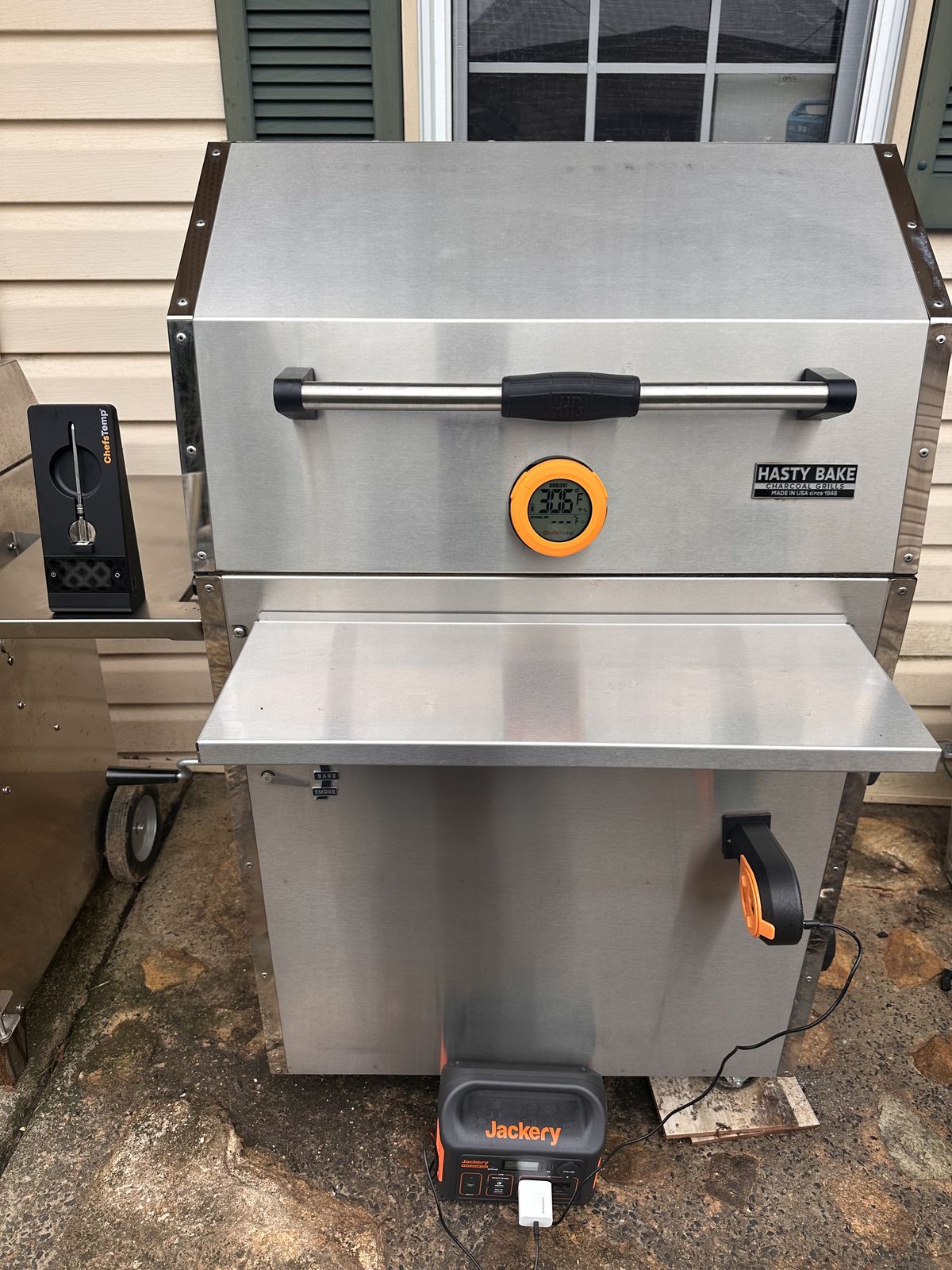 Stainless Hasty Bake charcoal grill with an orange digital thermometer and a portable power station beside it