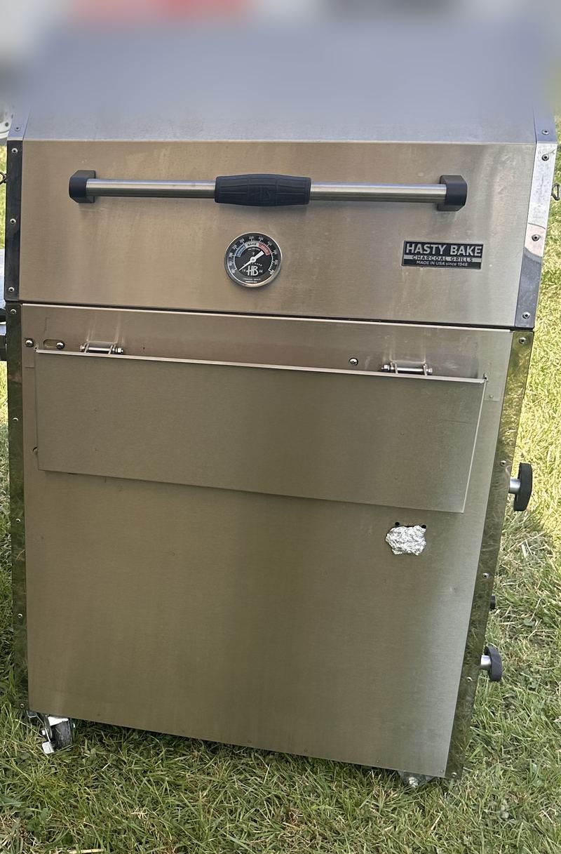The Hasty Bake 357, a stainless charcoal grill with its Hasty Bake badge and dial thermometer