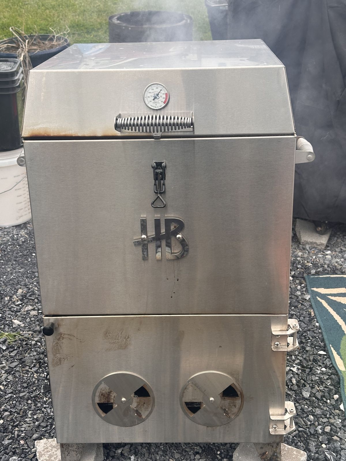 Stainless Hasty Bake charcoal smoker with HB logo, dial thermometer and two round vents