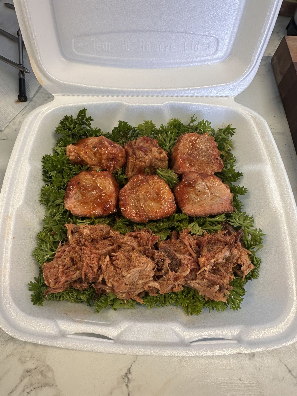 Glazed pork medallions and pulled pork on parsley in a takeout box