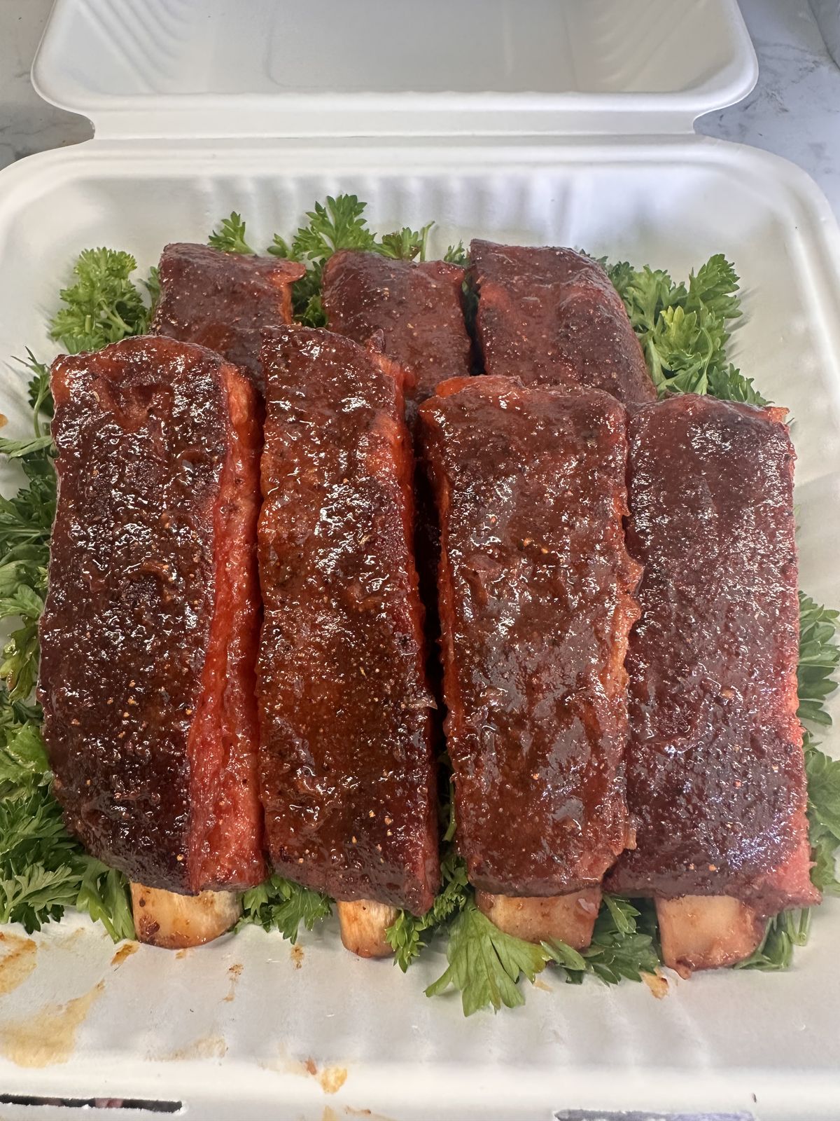 Glazed St. Louis-cut pork ribs in a takeout box on parsley