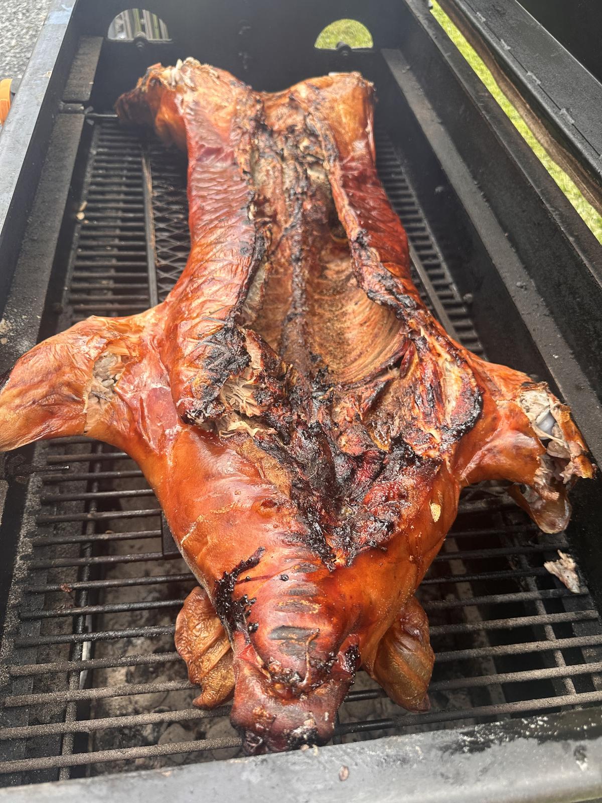 Whole roasted pig with deep mahogany skin resting on a smoker grate